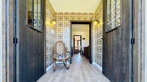 A hallway with patterned wallpaper, a wooden floor, and a rocking chair.