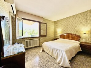 A hotel room with a bed, a window with a view, a radiator, and a small table with a lamp. - Can Bagudanch CostaBravaSi - Pool, A/C, Golf (Santa Cristina d'Aro)