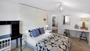 Quarto com cama, mesas de cabeceira, escrivaninha e espelho.