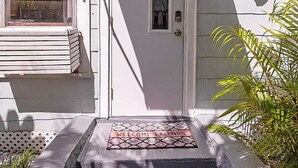 Uma casa branca com o número '2' na porta, um tapete de boas-vindas e um objeto decorativo na parede.