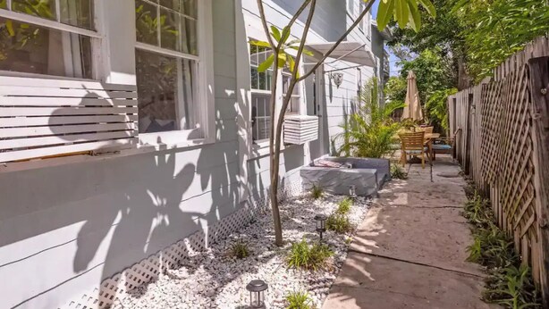 Um imóvel residencial com fachada branca, um pequeno jardim com pedriscos, uma cerca de madeira e um espaço de pátio com mesa e cadeiras.