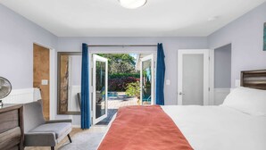 A bedroom with a large bed, a chair, a desk, and a view of a garden through an open door. - Enchanting Wilton Manors Haven: Outdoor Oasis (Wilton Manors)