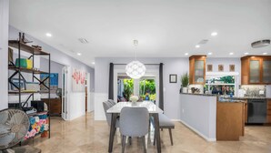 A modern kitchen with a central island, built-in cabinets, and a dining area with a white table and grey chairs. - Enchanting Wilton Manors Haven: Outdoor Oasis (Wilton Manors)
