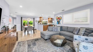 A modern living room with a grey sectional sofa, a coffee table, and a patterned rug. There is a dining area with a table and chairs, and a kitchen in the background. - Enchanting Wilton Manors Haven: Outdoor Oasis (Wilton Manors)