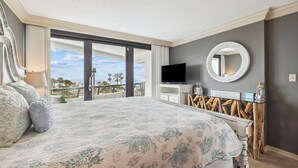 Un dormitorio con una cama grande, televisión, espejo y vista a la playa.