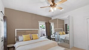 Un dormitorio con cama, mesita de noche, espejo, ventilador de techo y vistas al exterior.