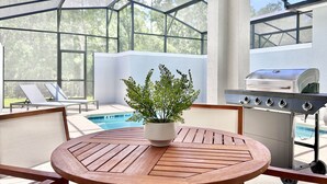 Ein überdachter Außenbereich mit Pool, Liegestühlen, einem Holztisch und einem Grill.