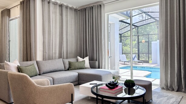 Ein modernes Wohnzimmer mit einem Ecksofa, einem Glastisch und Blick auf einen Außenpool.