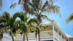 A two-story building with a balcony and a fenced garden area. - Ocean Pearl On The Beach Villa , ManOWar Cay, Abaco, Bahamas (Man-O-War Cay)