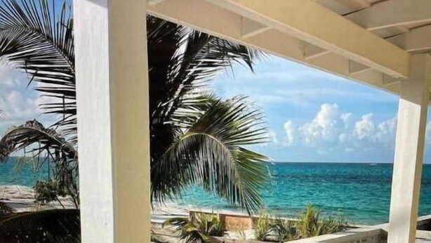 A beach view from a covered area with a wooden deck and white railings. - Ocean Pearl On The Beach Villa , ManOWar Cay, Abaco, Bahamas (Man-O-War Cay)