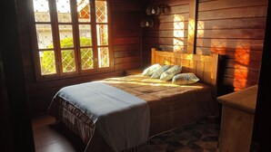 Una habitación de madera con una cama, un ventanal y una mesita de noche.