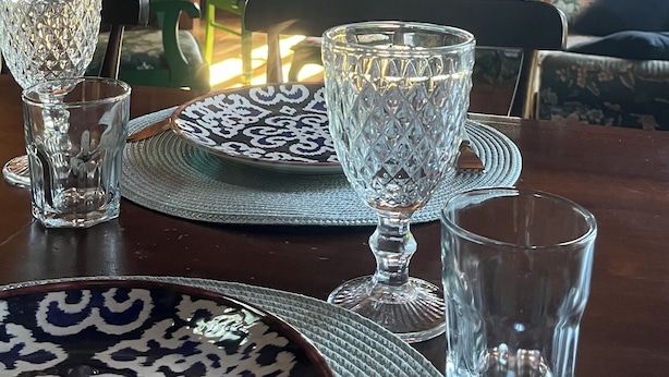 Un comedor con techo de madera, una araña y una mesa con platos, vasos y un jarrón.