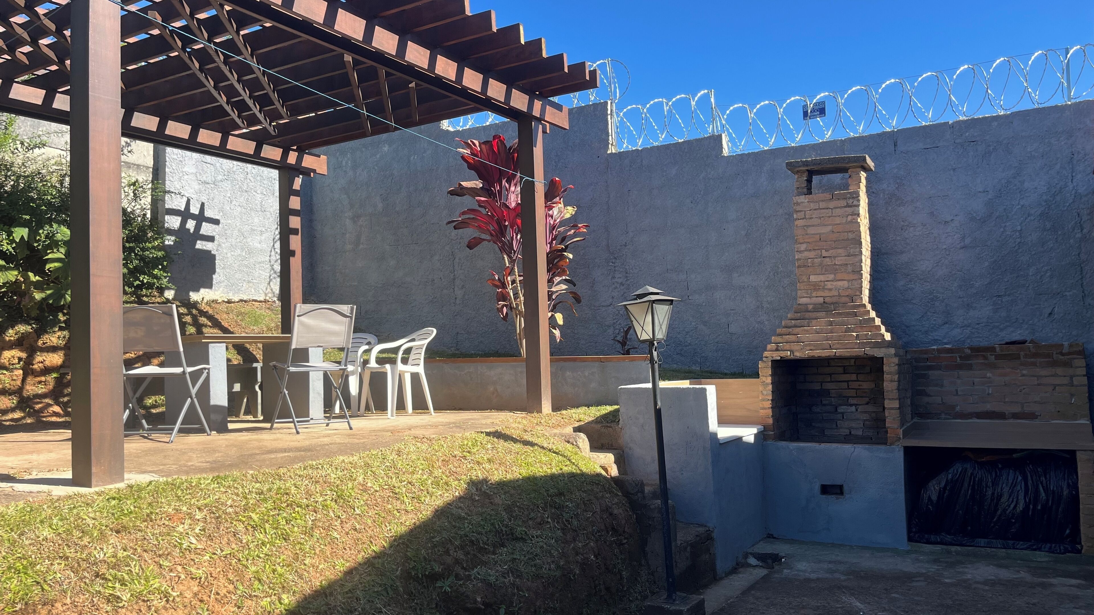 A patio area with a pergola, outdoor seating, a brick fireplace, and a barbed wire fence.