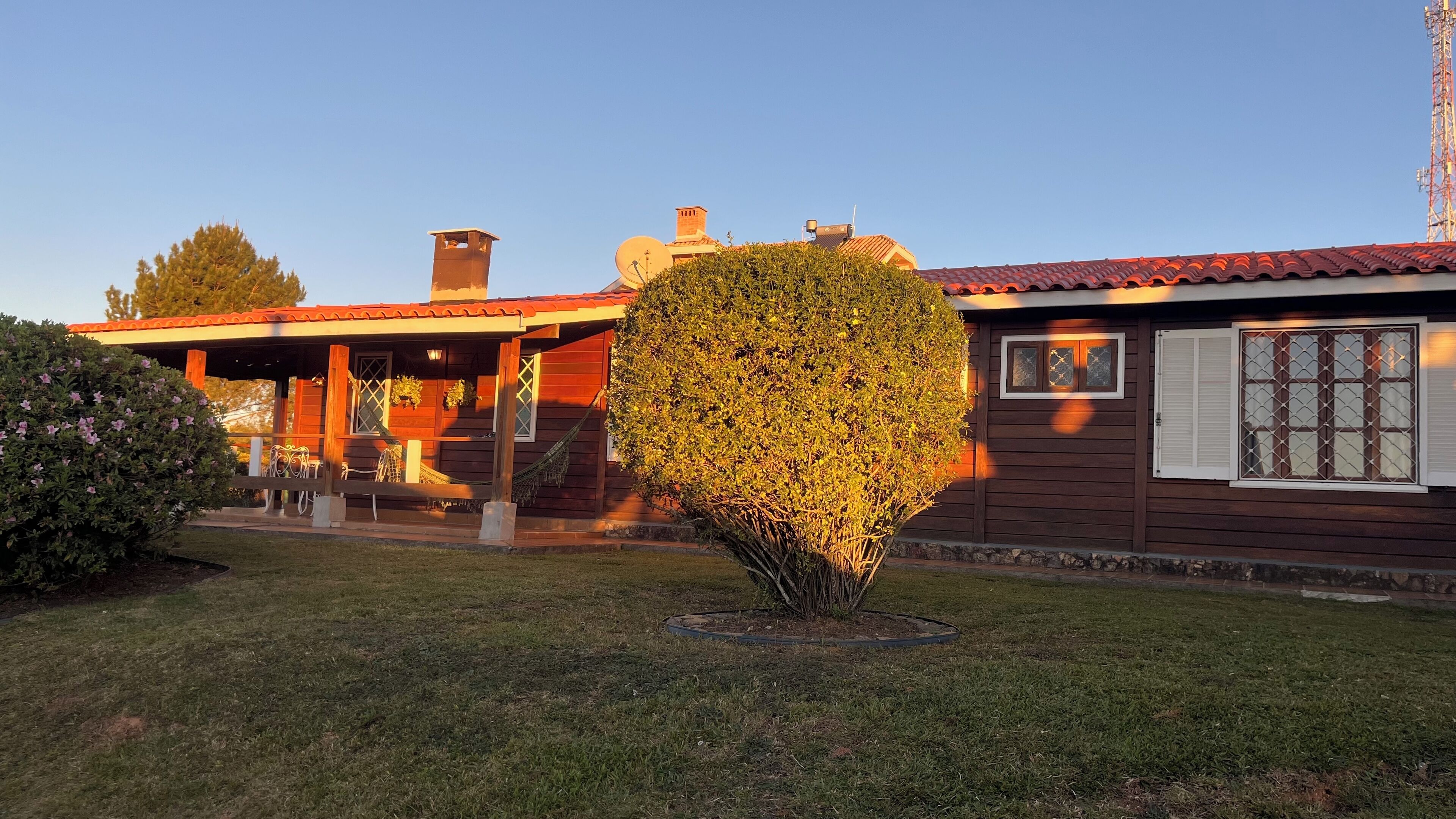 A wooden house with a red roof, a covered porch, and a well-maintained garden.