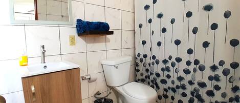 A bathroom with a toilet, sink, and mirror. There is a blue towel on a shelf and a trash can.