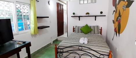 Een slaapkamer met een bed, een televisie, een bureau, een raam met gordijnen en een decoratie aan de wand.