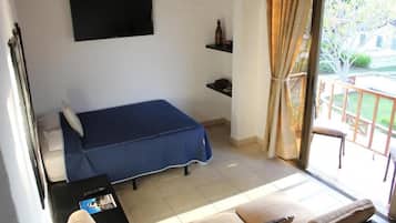 Una habitación con cama, sofá, televisión montada en la pared y balcón con vistas al exterior.