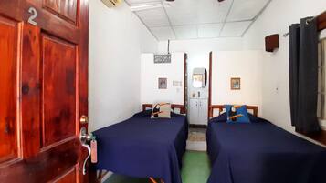 A room with two beds, a wooden door with a number, a small kitchenette, and a window with curtains.