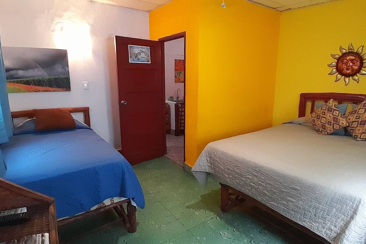 A room with two beds, a wooden headboard, a door, and a wall with a sun decoration.