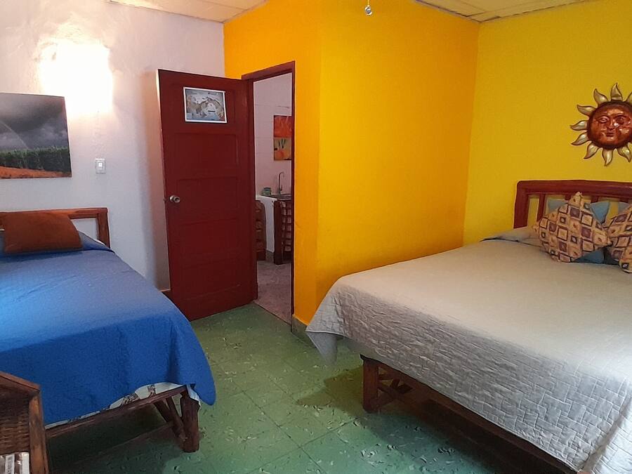 A room with two beds, a wooden headboard, a door, and a wall with a sun decoration.