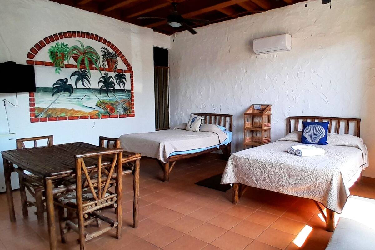 A room with two beds, a wooden table, and a mural on the wall.