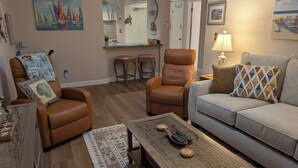 A living room with a brown leather armchair, a grey sofa, a wooden coffee table, and a patterned rug. - Bridget's Beach Retreat, On the beach with views on balcony,bedroom,living room (New Smyrna Beach)