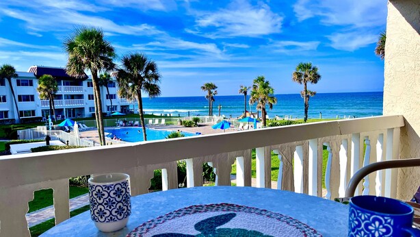 A balcony with a view of a swimming pool, palm trees, and a beach. - Bridget's Beach Retreat, On the beach with views on balcony,bedroom,living room (New Smyrna Beach)