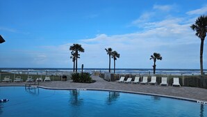 A swimming pool with lounge chairs and palm trees, overlooking the ocean. - Bridget's Beach Retreat, On the beach with views on balcony,bedroom,living room (New Smyrna Beach)