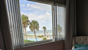 A hotel room with a bed, a window with curtains, and a view of the beach and ocean. - Bridget's Beach Retreat, On the beach with views on balcony,bedroom,living room (New Smyrna Beach)