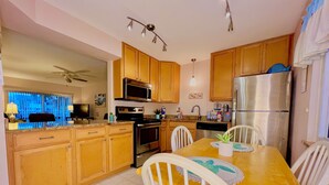 A modern kitchen with wooden cabinets, stainless steel appliances, and a dining area with a wooden table and white chairs. - Bridget's Beach Retreat, On the beach with views on balcony,bedroom,living room (New Smyrna Beach)