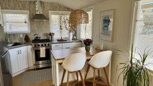A modern kitchen with white cabinets, a stainless steel stove, and a large window with blinds.