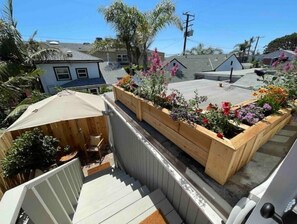 Un jardin sur le toit, agrémenté de jardinières en bois remplies de fleurs aux couleurs vives, d’un espace salon abrité et d’une vue sur les maisons voisines.