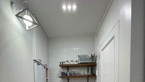 Une petite cuisine équipée d’un lave-linge, d’un évier et d’étagères en bois au-dessus.