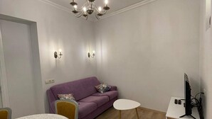 Un salon moderne avec un canapé violet, une table blanche et un téléviseur posé sur un meuble blanc.