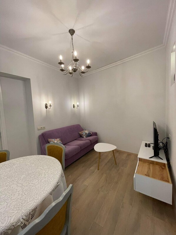 Un soggiorno moderno con un divano viola, un tavolo bianco e una TV su un mobile bianco.