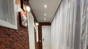 Un couloir aux murs en briques, au plancher en bois, aux rideaux blancs et doté d’un éclairage encastré.