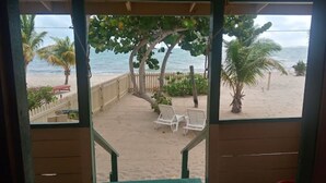 Vista de la playa desde un área techada con dos sillas blancas y una valla de madera.