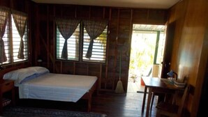 Una habitación con dos camas, piso de madera, un escritorio con silla y una ventana con cortinas.