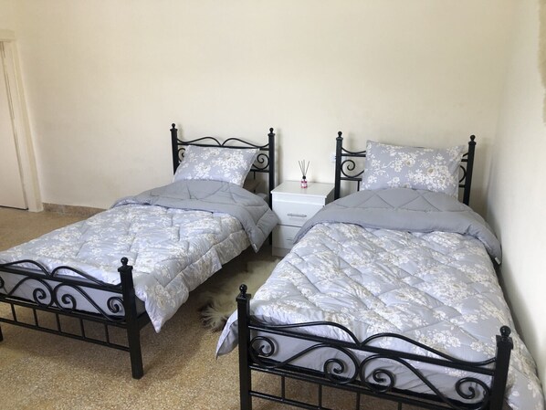 Two single beds with black frames and floral-patterned duvets, accompanied by a bedside table with a drawer.
