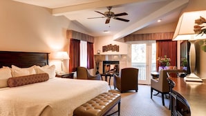 A hotel room with a large bed, a desk, a chair, a fireplace, and a balcony with curtains.