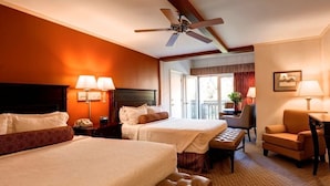 A hotel room with two beds, a ceiling fan, a desk, a chair, and a balcony with a view.