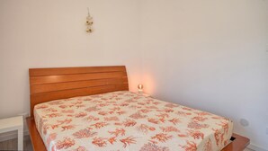 Ein Schlafzimmer mit einem hölzernen Kopfteil, einem Bett mit einem Korallenmuster-Bettüberwurf, einem Nachttisch und einer wandmontierten Leuchte.