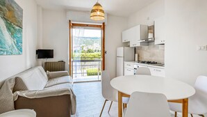 Eine moderne Küche mit weißen Schränken und einem Gasherd, ein Essbereich mit einem runden Tisch und Stühlen, eine Couch mit gestreiften Kissen und ein Balkon mit Stadtblick.