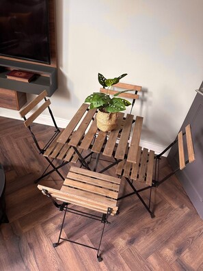 A foldable wooden table with a woven basket containing a plant, set against a wall with a television and a book on a shelf. - Stylish modern bright and airy flat in South West London - Putney (London)