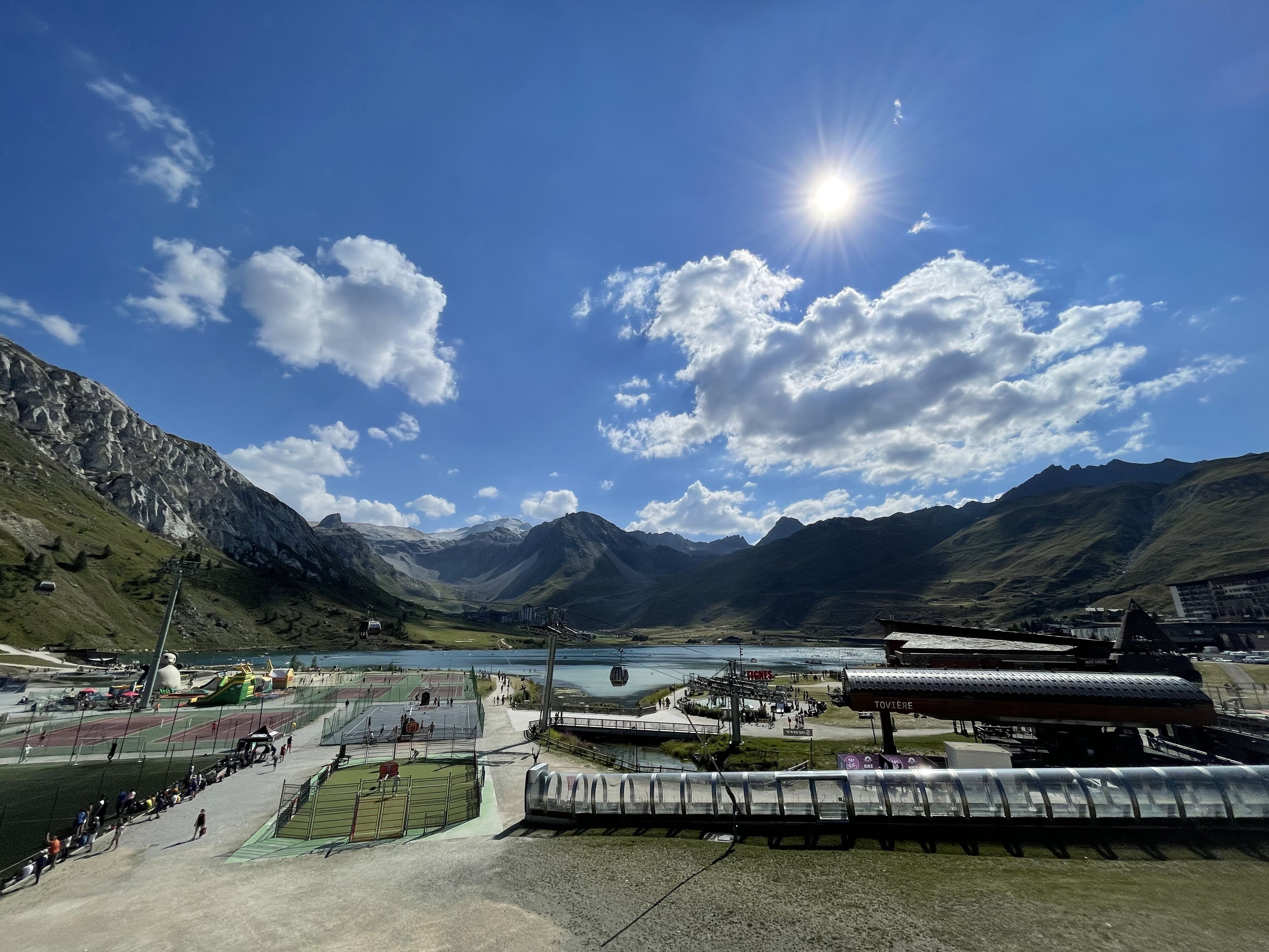 Un paysage montagneux avec un ciel dégagé, un lac et une station de ski dotée de pistes balisées et d’un téléphérique.