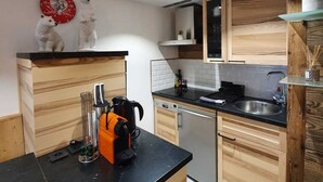 A modern kitchen with wooden cabinets, a black countertop, and a red clock on the wall. - Studio Moderne Spacieux Avec VUE Imprenable ! (Tignes)