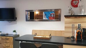A modern kitchen with a wooden island, two black bar stools, a flat-screen TV mounted on the wall, and a red and white clock with a bear design. - Studio Moderne Spacieux Avec VUE Imprenable ! (Tignes)