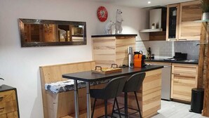 A modern kitchen with wooden cabinets, a dining area with a brown leather ottoman, and a small round table. - Studio Moderne Spacieux Avec VUE Imprenable ! (Tignes)