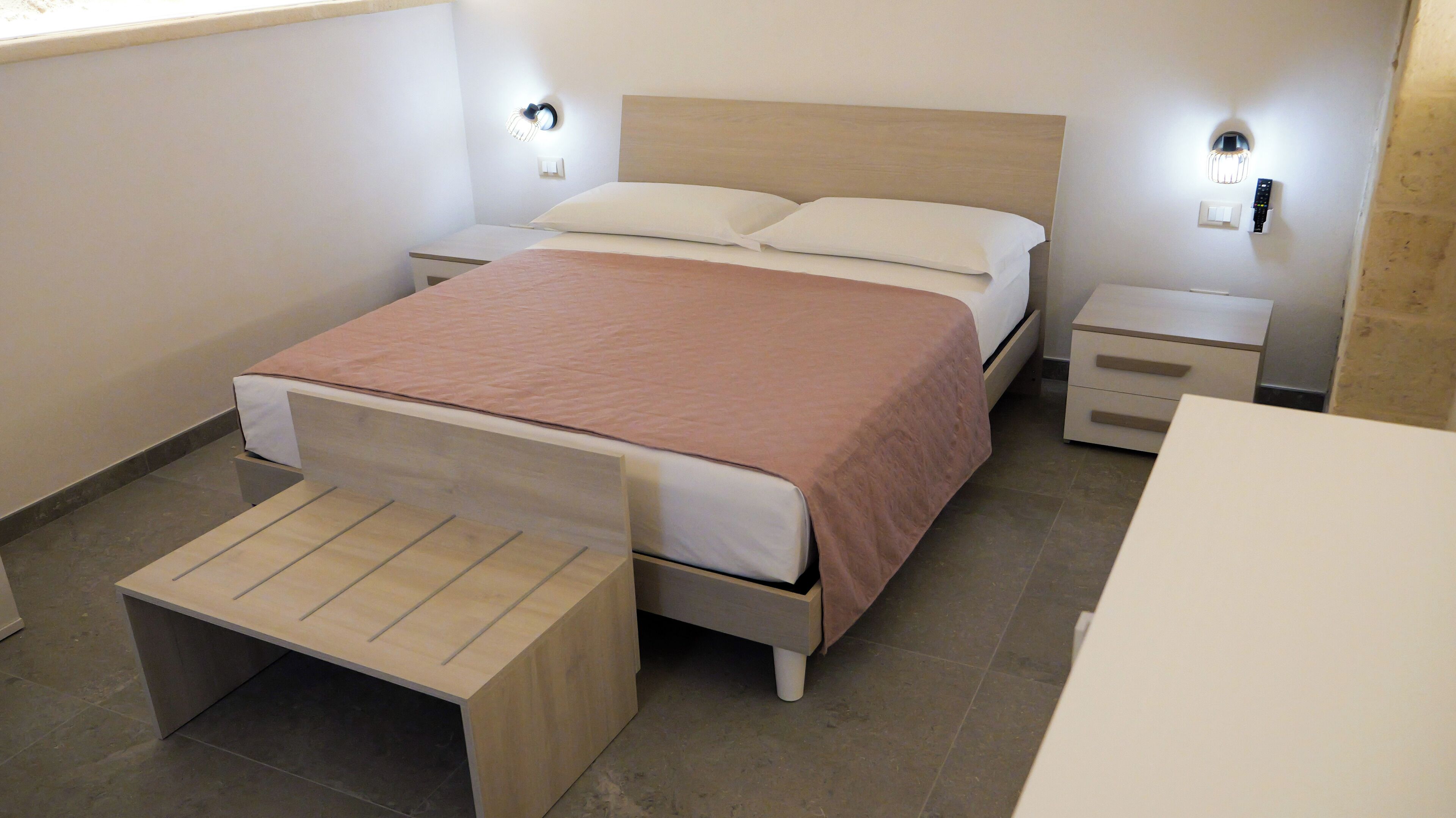 Ein modernes Schlafzimmer mit einem hölzernen Bett, Nachttischen, einer Bank und Wandleuchten.