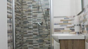 Un baño moderno con ducha de vidrio, tocador de madera y salpicadero de azulejos.